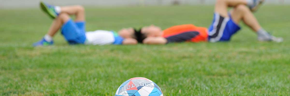 kids lying in grass beside soccer ball